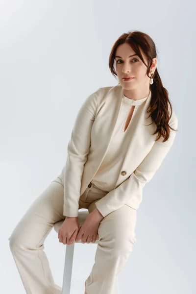 Beautiful woman in formal wear looking at camera while sitting on chair isolated on grey — Stock Photo