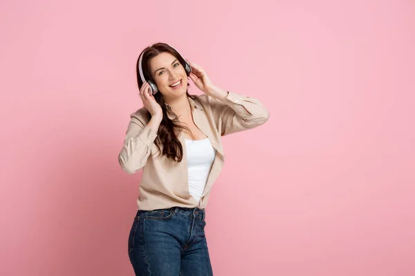 Mulher positiva ouvindo música em fones de ouvido no fundo rosa — Fotografia de Stock