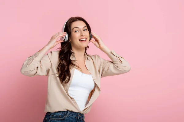 Mulher alegre em fones de ouvido olhando para o fundo rosa — Fotografia de Stock