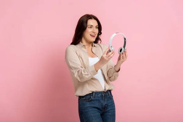 Positive brunette woman holding headphones on pink background — Stock Photo