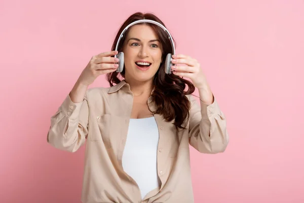 Positive woman holding wireless headphones on pink background — Stock Photo