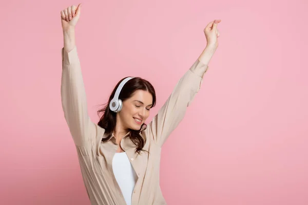 Mujer atractiva en auriculares bailando con los ojos cerrados sobre fondo rosa - foto de stock