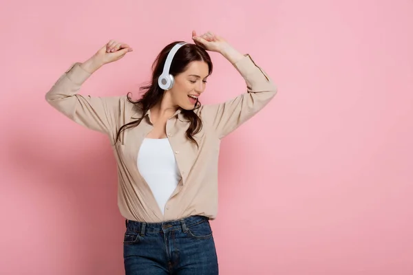 Hermosa mujer en auriculares bailando y cantando sobre fondo rosa - foto de stock
