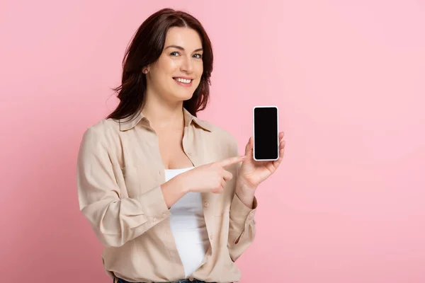Smiling woman pointing with finger at smartphone on pink background, concept of body positive — Stock Photo