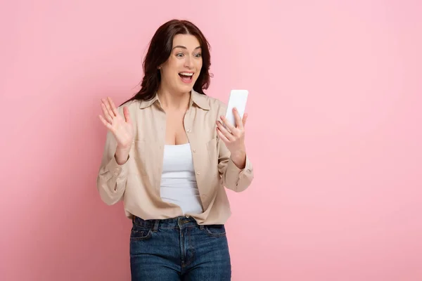 Cheerful woman having video call on smartphone on pink background, concept of body positive — Stock Photo