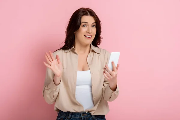 Lächelnde Frau schaut in die Kamera, während sie Videoanrufe auf dem Smartphone auf rosa Hintergrund hat — Stockfoto