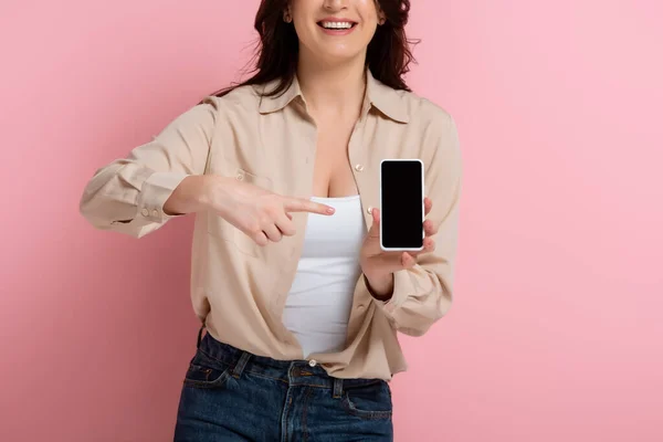 Cropped view of smiling woman pointing with finger at smartphone on pink background — Stock Photo
