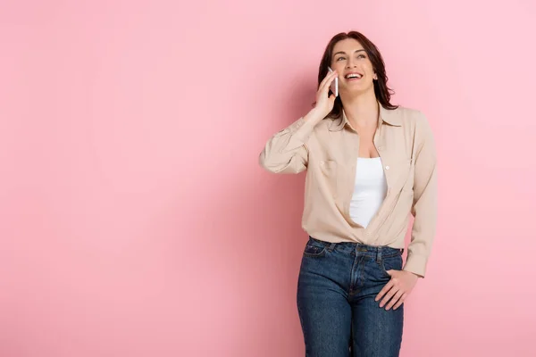 Positive woman smiling while talking on cellphone on pink background — Stock Photo