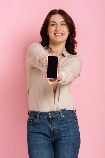 Выборочный фокус красивой брюнетки женщина показывает смартфон на розовом фоне — стоковое фото