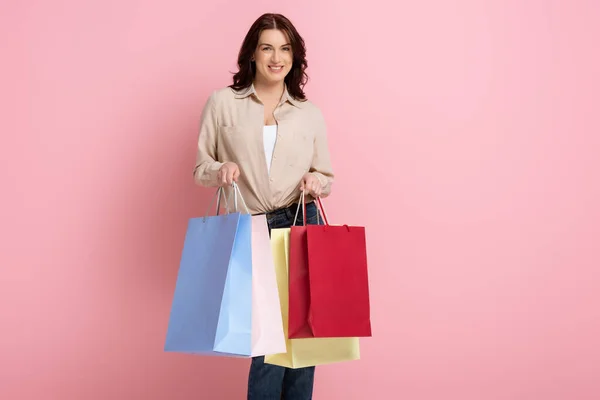 Красива жінка посміхається, тримаючи барвисті сумки для покупок на рожевому фоні — стокове фото