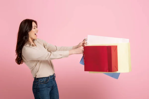 Side view of cheerful woman holding shopping bags on pink background, concept of body positive — Stock Photo