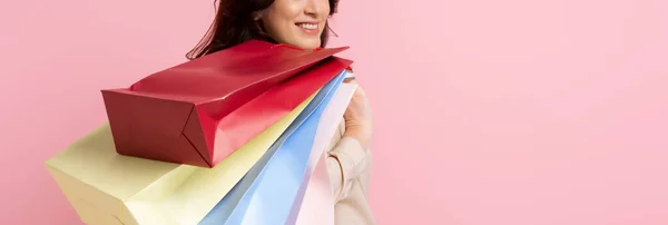 Panoramic crop of smiling woman holding shopping bags isolated on pink — Stock Photo