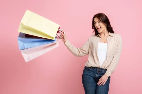Attraktive, fröhliche Frau, die in die Kamera lächelt, während sie Einkaufstüten isoliert auf rosa hält, Konzept des positiven Körpers — Stockfoto