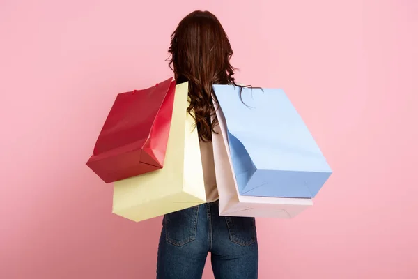 Vue arrière de la femme brune tenant des sacs à provisions sur fond rose — Photo de stock