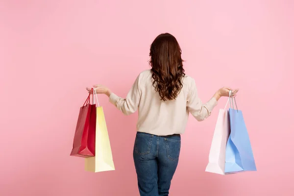 Вид ззаду жінка тримає барвисті сумки для покупок ізольовані на рожевому — стокове фото