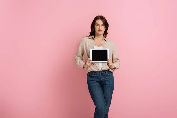 Mulher morena atraente segurando tablet digital com tela em branco no fundo rosa, conceito de corpo positivo — Fotografia de Stock