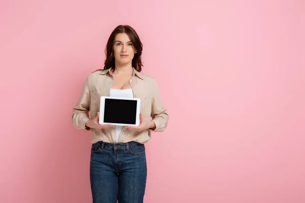Жінка з Брюнета дивиться на камеру, тримаючи цифровий планшет на рожевому фоні. — стокове фото