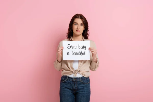 Hermosa mujer de la celebración de la tarjeta con cada cuerpo es hermoso letras sobre fondo rosa - foto de stock