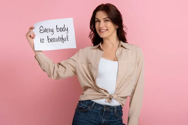 Attraente bruna donna in possesso di carta con ogni corpo è bella lettering su sfondo rosa — Foto stock