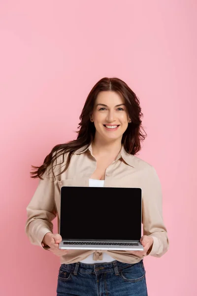 Bella donna sorridente che mostra laptop con schermo bianco isolato su rosa — Foto stock