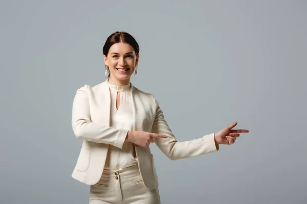 Smiling woman in formal wear pointing with fingers isolated on grey — Stock Photo