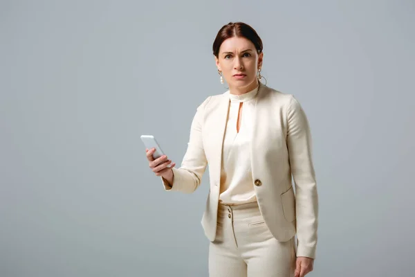 Confused businesswoman looking at camera while holding smartphone isolated on grey — Stock Photo