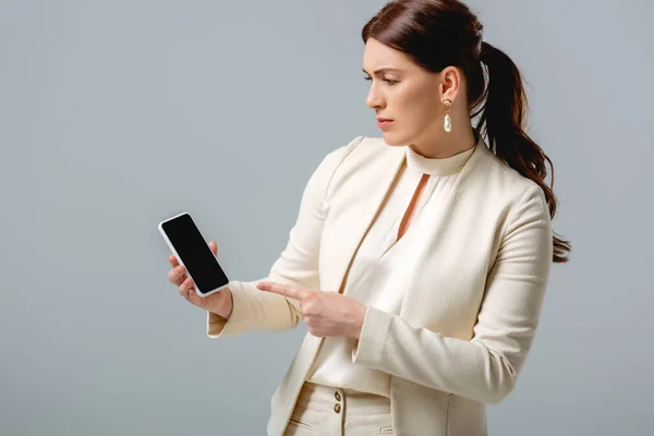 Bella donna in abito formale che punta con il dito allo smartphone isolato sul grigio — Foto stock