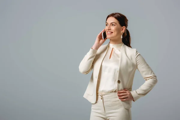 Attrayant femme en tenue formelle souriant tout en parlant sur smartphone isolé sur gris — Photo de stock