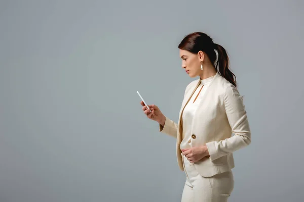 Side view of attractive businesswoman using smartphone isolated on grey — Stock Photo