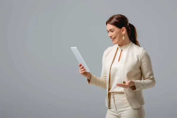 Bella donna d'affari sorridente mentre tiene tablet digitale isolato su grigio — Foto stock