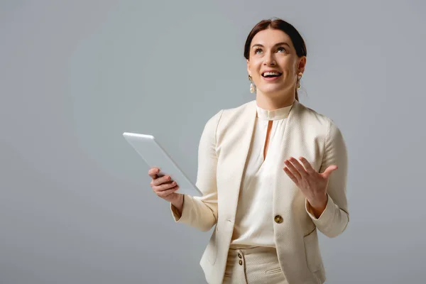 Mujer de negocios positiva mirando hacia arriba durante la videollamada en tableta digital aislada en gris - foto de stock
