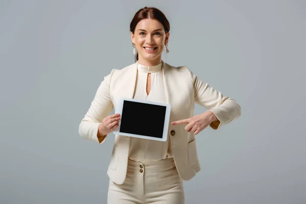 Bella donna d'affari sorridente che punta con il dito al tablet digitale isolato su grigio — Foto stock