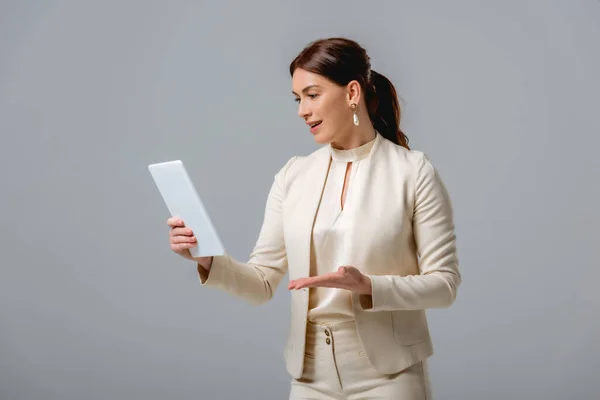 Hermosa mujer morena en ropa formal que tiene videollamada en tableta digital aislada en gris - foto de stock