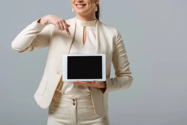 Vista recortada de una mujer de negocios sonriente apuntando a una tableta digital aislada en gris - foto de stock