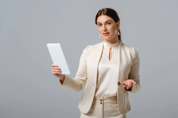 Приваблива бізнес-леді, що вказує рукою і тримає цифровий планшет ізольовано на сірому — стокове фото