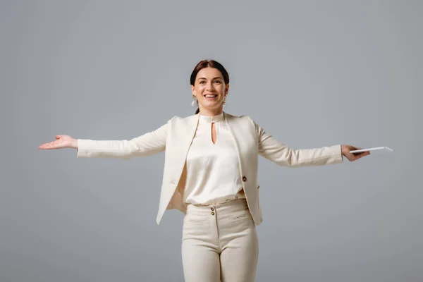 Mulher sorridente bonita em desgaste formal segurando tablet digital e apontando com a mão isolada em cinza — Fotografia de Stock