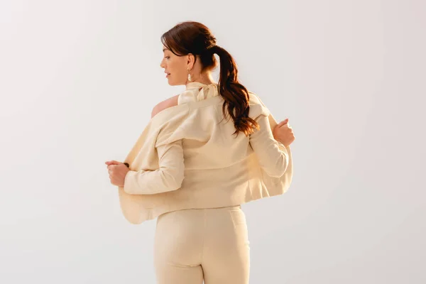 Вид на красивую деловую женщину, снимающую куртку, изолированную на сером — стоковое фото