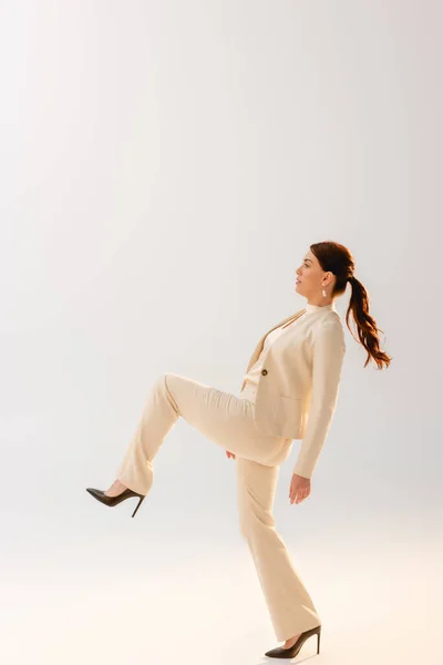 Vista lateral da mulher morena no desgaste formal e saltos no fundo cinza — Fotografia de Stock