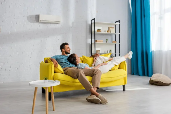 Lächelnde Frau liegt neben gutaussehendem Mann auf gelbem Sofa zu Hause — Stockfoto