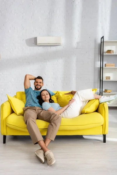 Hermosa mujer tumbada en el sofá cerca de hombre guapo sonriendo a la cámara - foto de stock