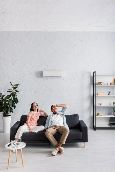 Young couple feeling hot while sitting on sofa at home — Stock Photo