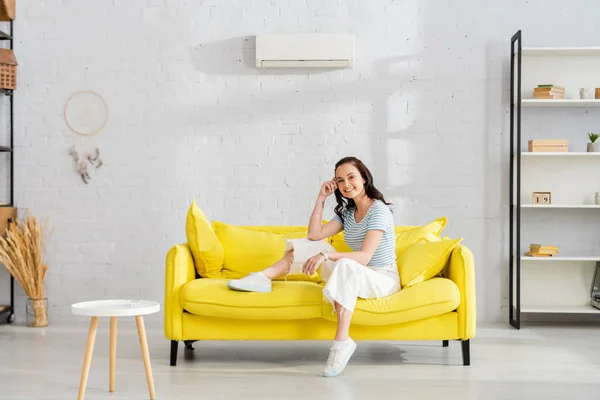 Hermosa mujer sonriendo a la cámara mientras está sentada en el sofá en la sala de estar - foto de stock