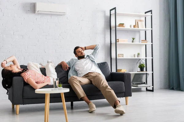 Casal cansado sofrendo de calor no sofá na sala de estar — Fotografia de Stock