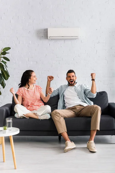 Lächelndes Paar zeigt Ja-Geste im Sitzen unter Klimaanlage auf Sofa — Stockfoto