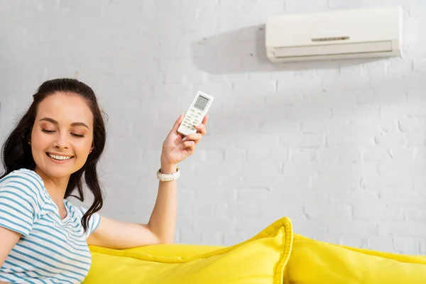 Focus selettivo di bella donna sorridente in possesso di telecomando del condizionatore d'aria a casa — Foto stock