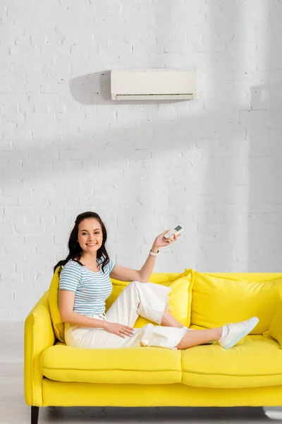 Muchacha sonriente atractiva sosteniendo el mando a distancia del aire acondicionado en la sala de estar - foto de stock