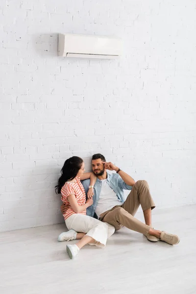 Hombre guapo abrazando novia mientras están sentados juntos en el suelo bajo el aire acondicionado - foto de stock