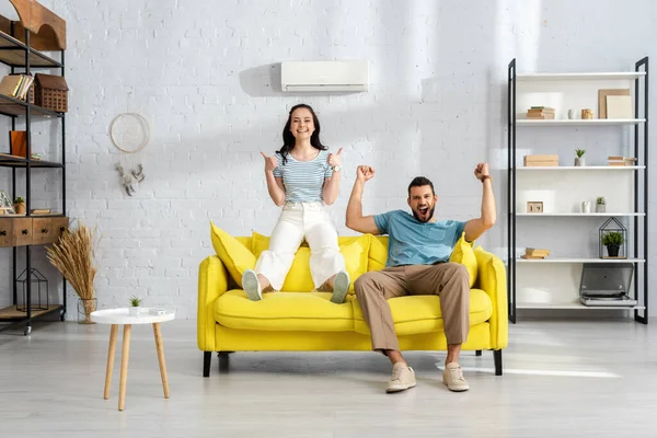 Positive couple showing thumbs up and yeah gestures on couch in living room — Stock Photo