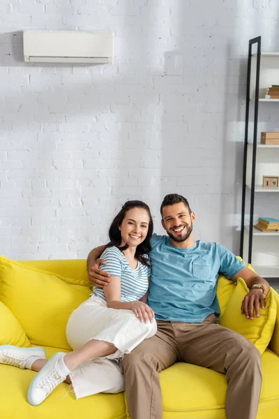 Schöne Frau lächelt in die Kamera, während sie zu Hause auf dem Sofa neben ihrem Freund sitzt — Stockfoto