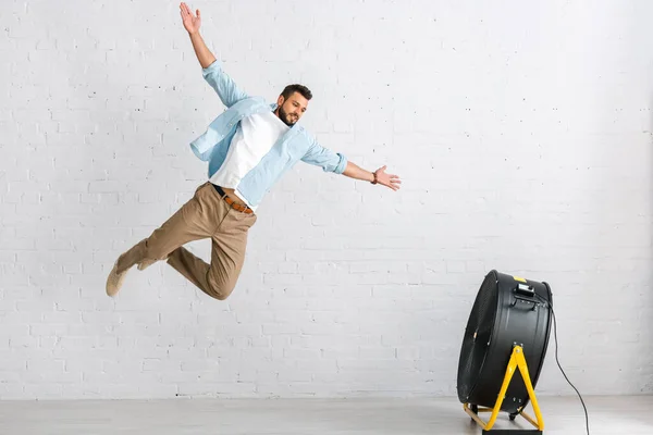 Красивий бородатий чоловік стрибає біля електричного вентилятора вдома — стокове фото
